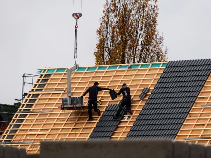 Dachdecker decken ein Steildach neu ein, ein Kran liefert die Ziegel