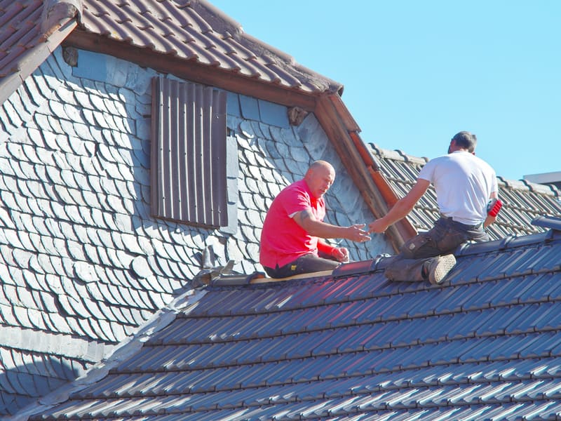 Zwei Dachdecker arbeiten auf einem Schieferdach mit Gaube