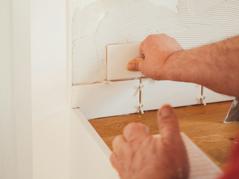 Hand setzt eine Fliese mit Fliesenkreuzen in das Kleberbett